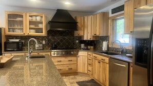 Cocina moderna con encimeras de granito, electrodomésticos de acero inoxidable, armarios de madera y una campana extractora negra.