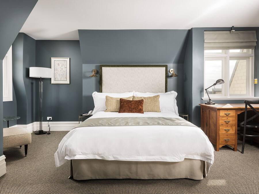 A bedroom with a large bed, a desk, a chair, a lamp, and a window with a view of a building.