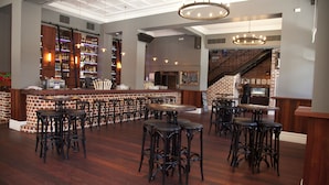 A spacious bar area with multiple seating options, a brick accent wall, and a staircase leading to an upper level. - The National Hotel (Fremantle)