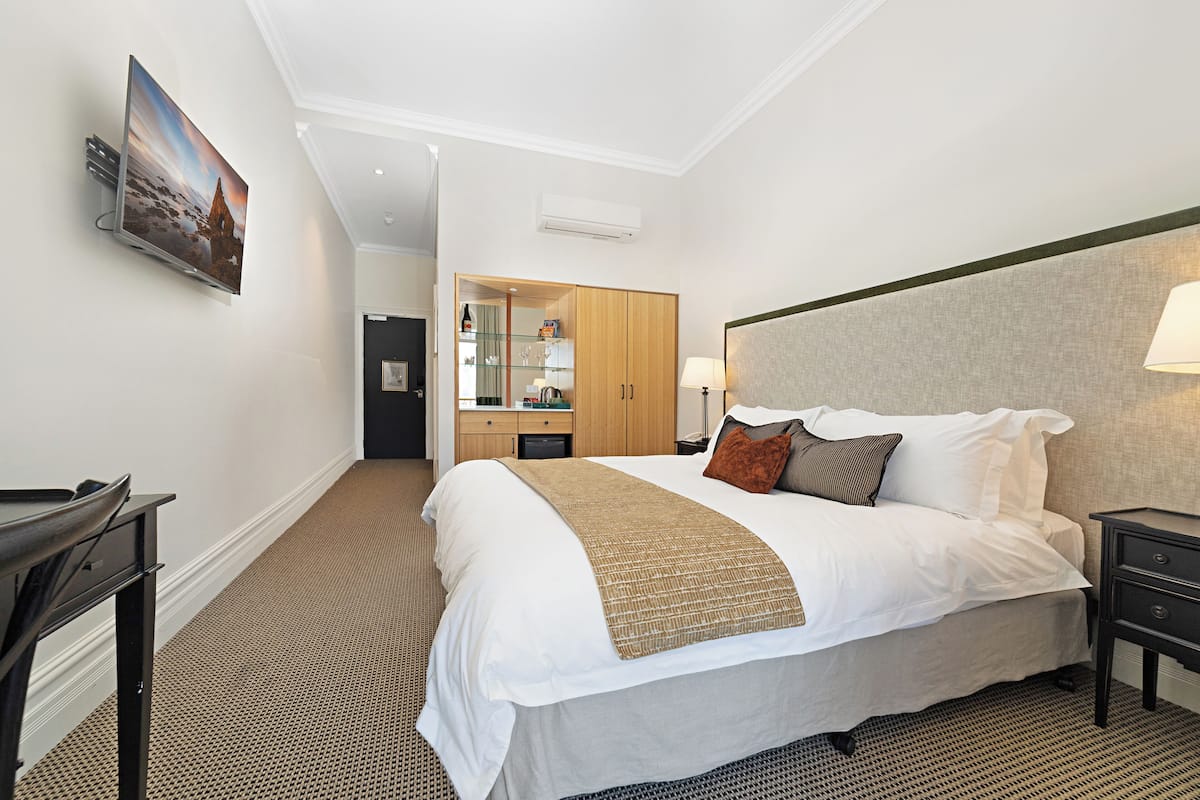 Une chambre d’hôtel avec un grand lit, un bureau, une armoire et un téléviseur fixé au mur.