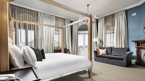 A four-poster bed with a telephone and a tray table, a dark sofa with cushions, and a large window with curtains. - The National Hotel (Fremantle)