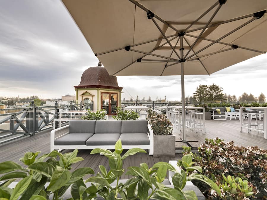 A rooftop terrace with a white sofa, a large umbrella, and potted plants.