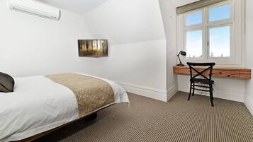 Ein Schlafzimmer mit Bett, Schreibtisch, Stuhl, Fenster und Klimaanlage.