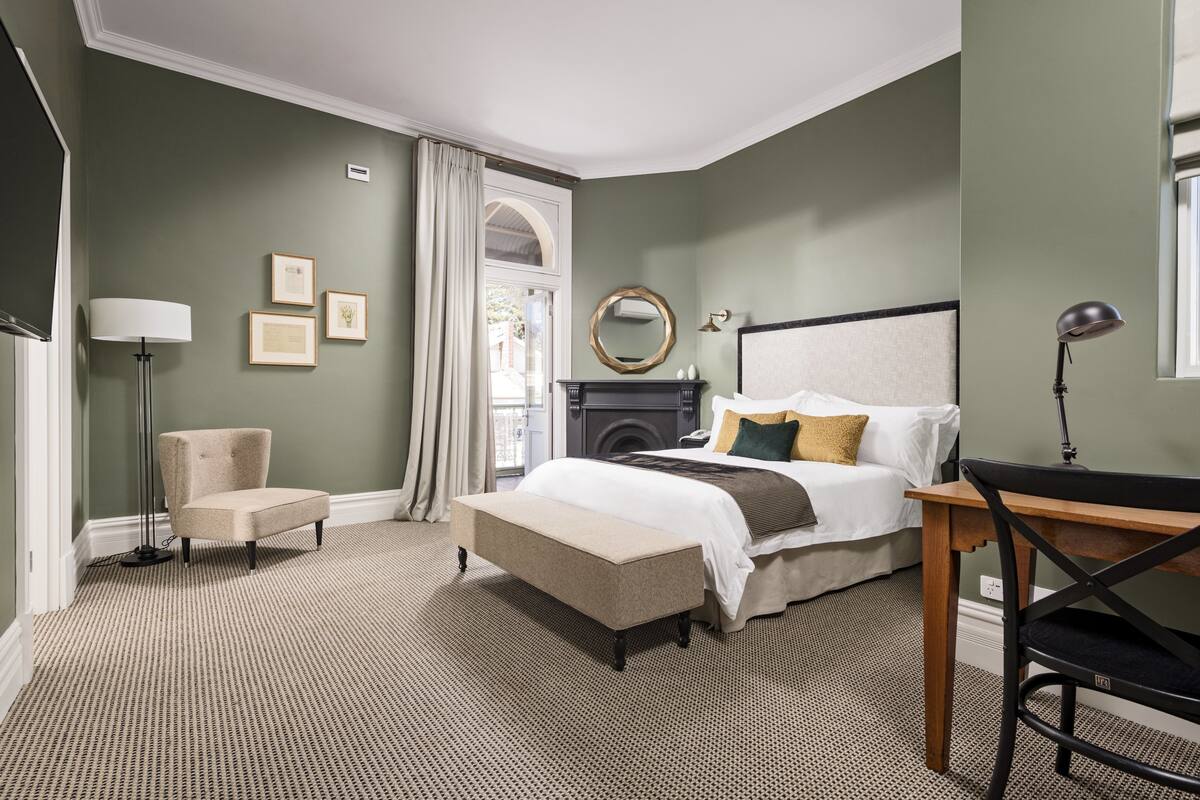 Une chambre à coucher avec un lit, une chaise, un bureau, une lampe et une cheminée.