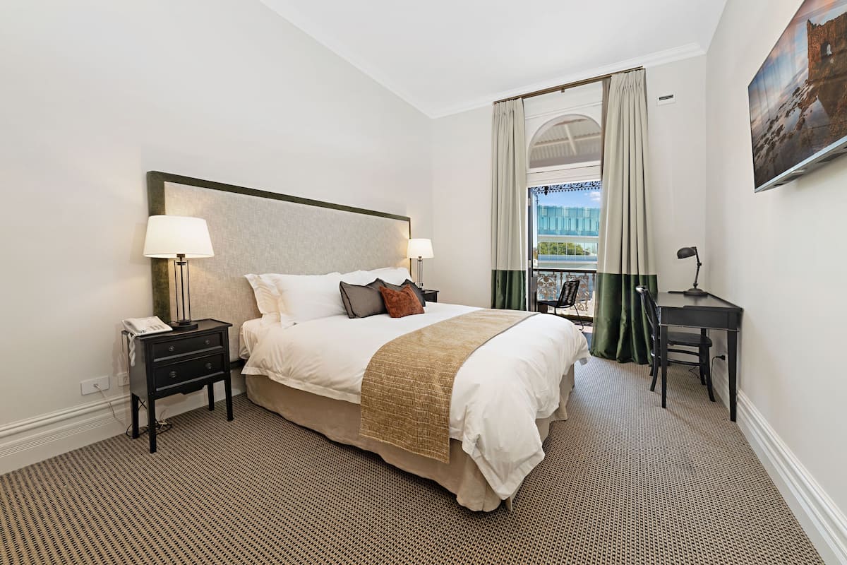 Une chambre d’hôtel avec un grand lit, des tables de chevet avec des lampes, un bureau et une vue sur un immeuble par une fenêtre avec des rideaux.