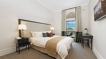 Habitación de hotel con una cama grande, mesitas de noche con lámparas, un escritorio y vista a un edificio a través de una ventana con cortinas.