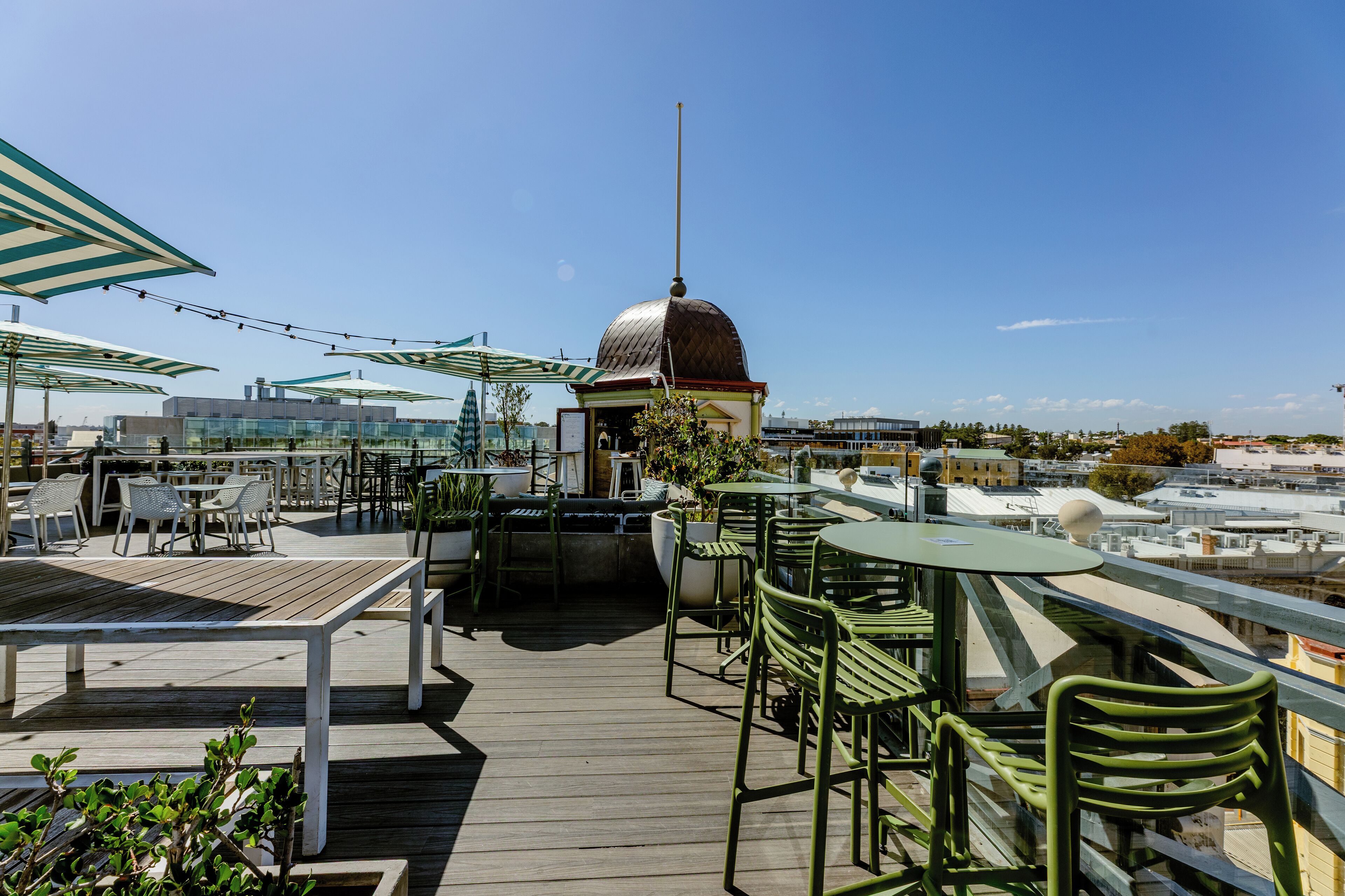 Terraza exterior con mesas y sillas, una estructura abovedada y vista panorámica de la ciudad.