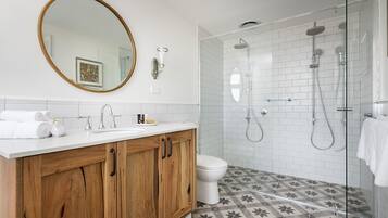 Un baño con tocador de madera, un espejo grande, inodoro y zona de ducha con puerta de cristal.