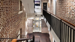A multi-level interior with exposed brick walls, wooden railings, and a staircase leading to an upper floor. - The National Hotel (Fremantle)