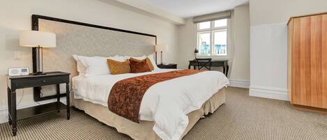 A hotel room with a large bed, a desk, a chair, and a wardrobe.