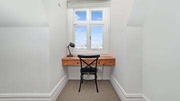 A small, bright room with a desk and chair, a window with a view, and a patterned floor.