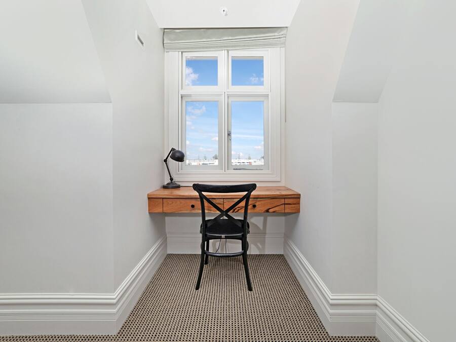 A small, bright room with a desk and chair, a window with a view, and a patterned floor.