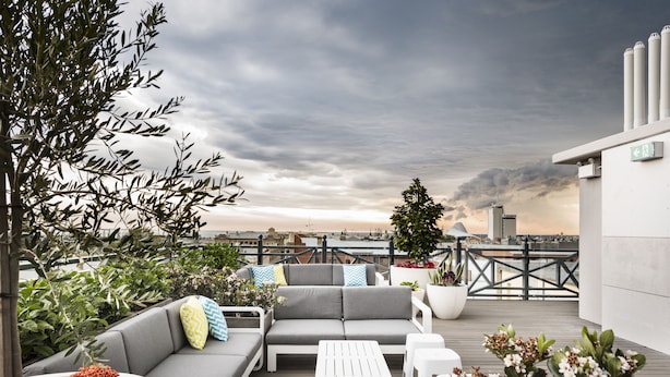 A rooftop terrace with a grey sofa set, white coffee table, and potted plants. - The National Hotel (Fremantle)
