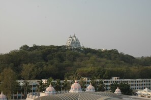 A temple complex with multiple domes on a hill, surrounded by trees and buildings. - Sai Towers (Puttaparti)