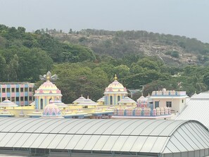 A series of colorful temple structures with domed roofs, surrounded by greenery and hills. - Sai Towers (Puttaparti)
