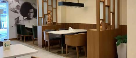 A restaurant with a modern interior, featuring a dining area with tables and chairs, a decorative wall with a framed picture, and a ceiling with linear lighting.
