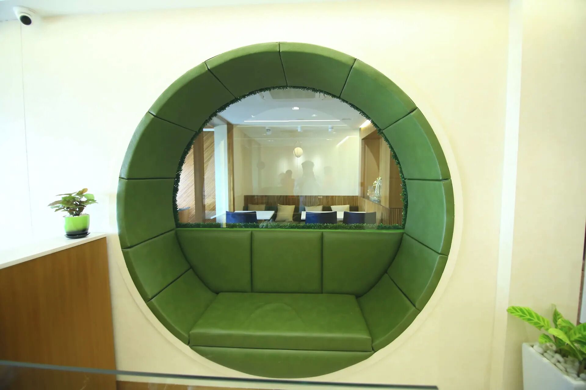 A circular green seating area with a reflective surface in the center, surrounded by a white wall.
