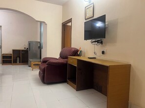 A room with a sofa, a desk, a television mounted on the wall, and a door leading to another room.