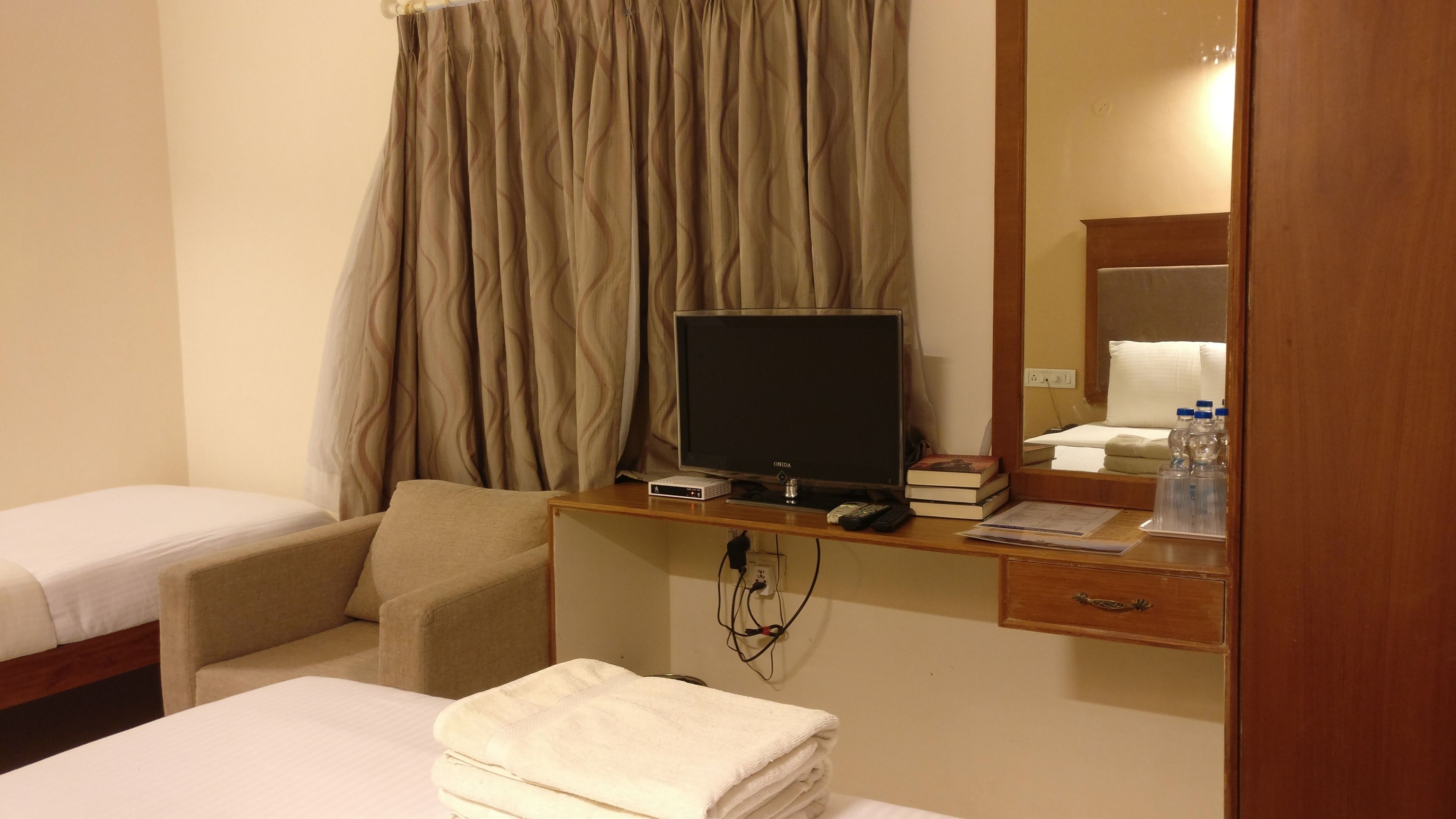 Habitación de hotel con una cama, un escritorio con computadora, una silla, televisor y espejo.
