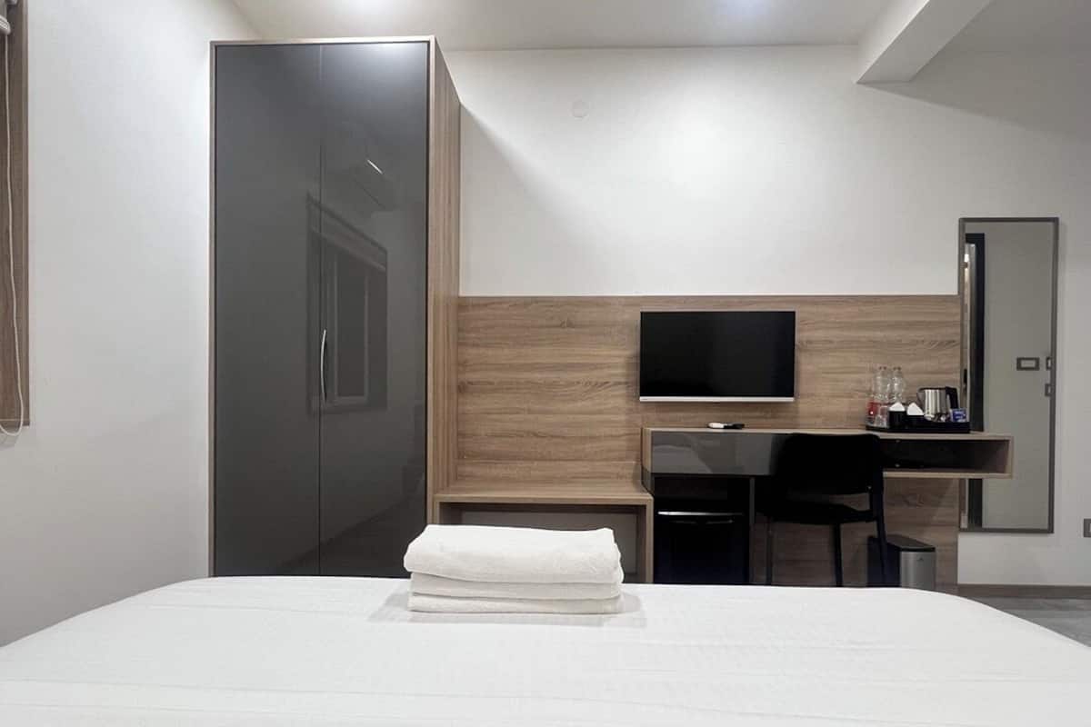 Une chambre d’hôtel comprenant un lit, un bureau avec une chaise, une télévision et une armoire.