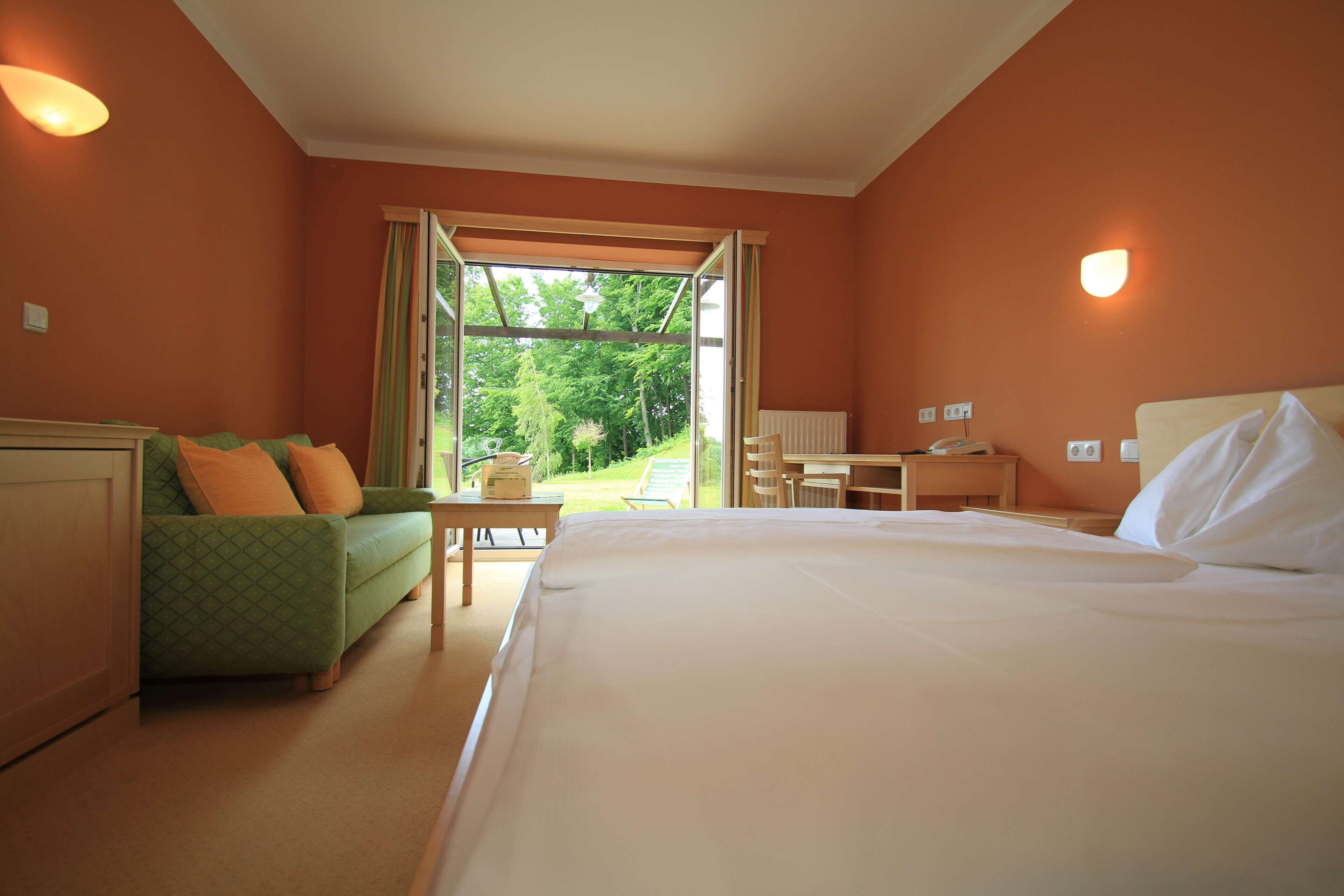 Habitación de hotel con cama, sofá verde, escritorio y vistas al exterior.