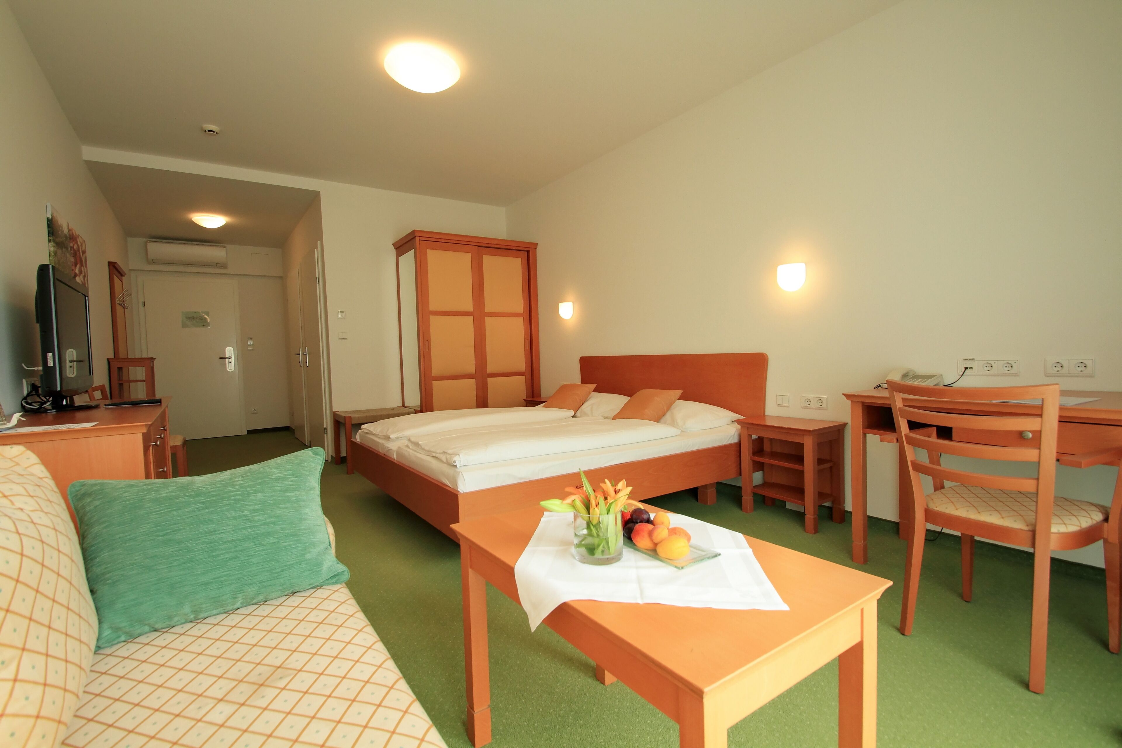 Habitación de hotel con cama, escritorio, silla, mesa con fruta y flores, y sofá.