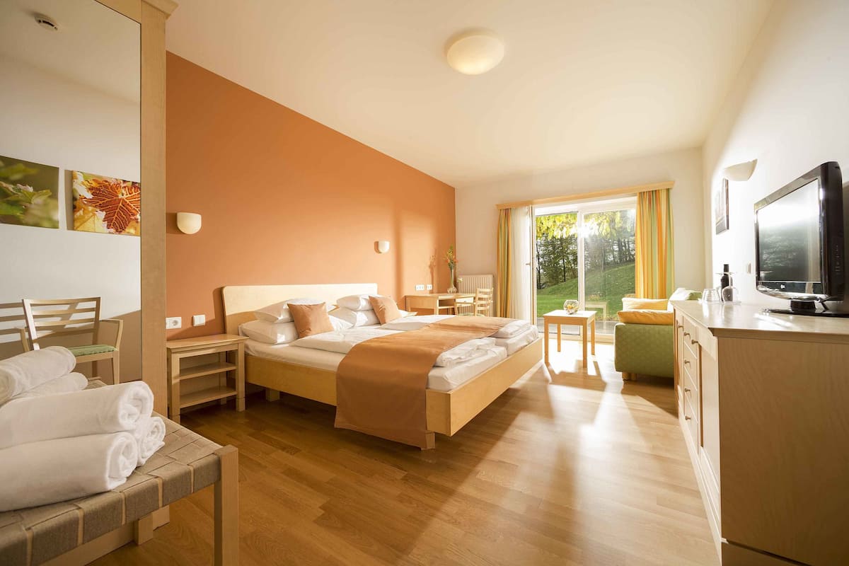 A hotel room with a bed, bedside tables, a desk, a chair, a television, and a view of the outdoors.