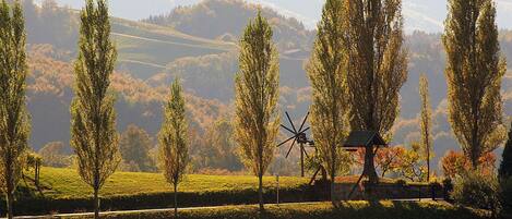 A windmill in a rural landscape with trees and hills in the background.