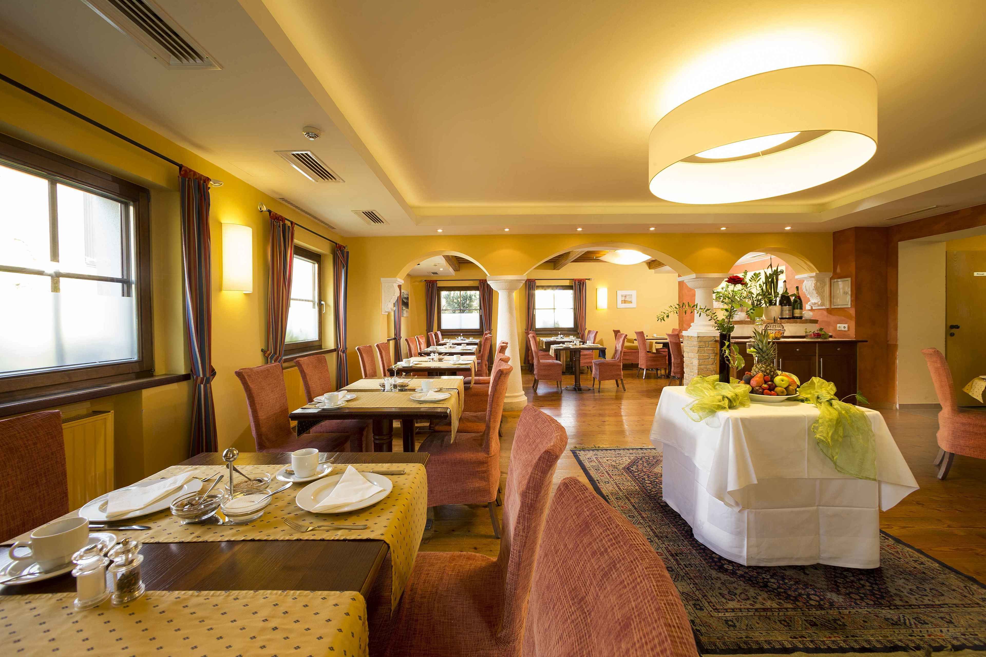 A hotel dining area with multiple tables, chairs, and a central table with a fruit display.