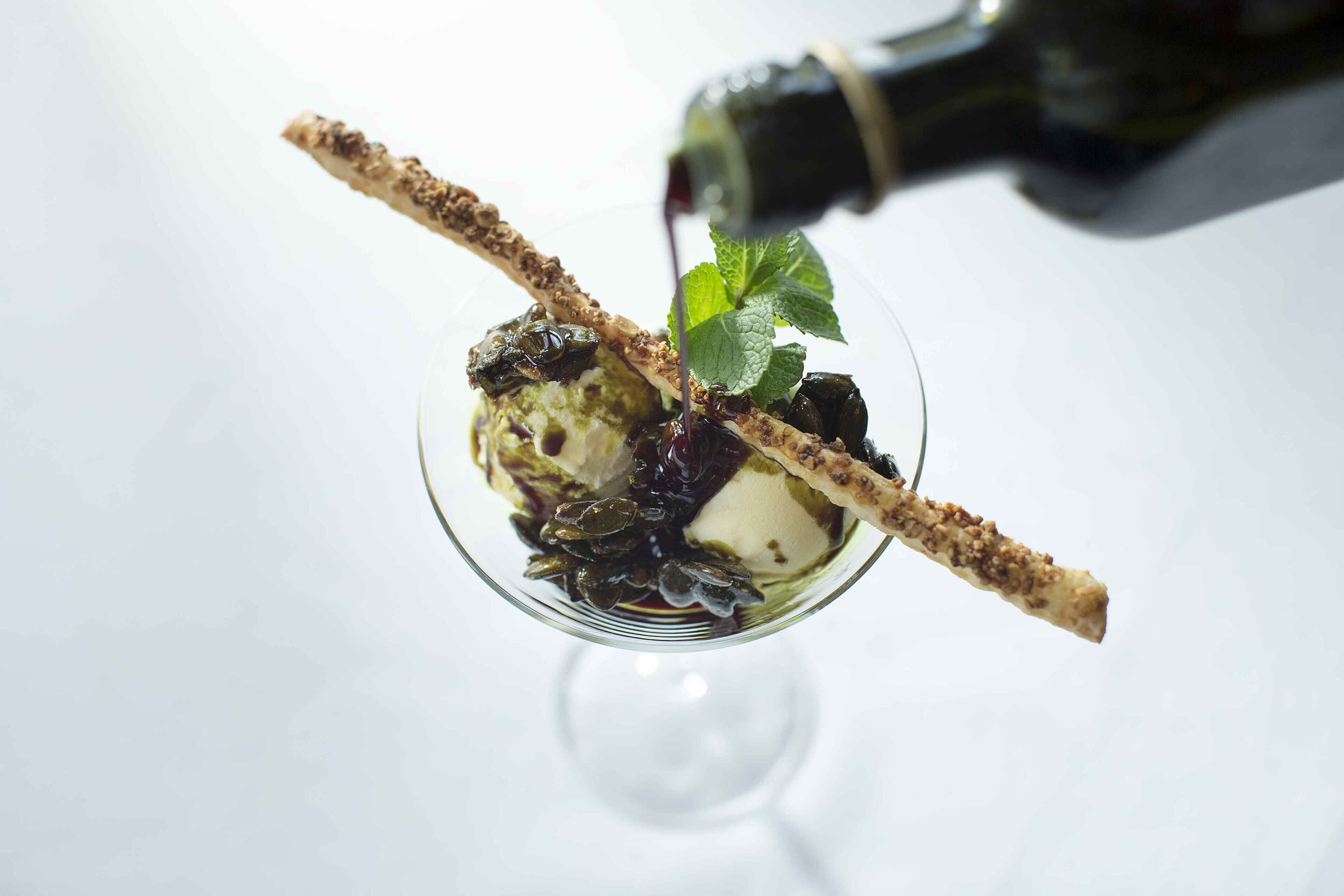 Un dessert servi dans un bol en verre, décoré d’une feuille de menthe et accompagné d’un bâtonnet enrobé de chocolat.