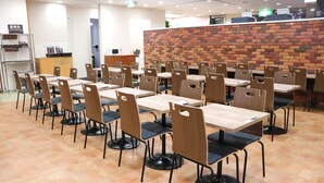 A cafeteria with multiple tables and chairs, a brick wall, and a counter with a computer. - FUN GATE HOTEL SAPPORO (Sapporo)