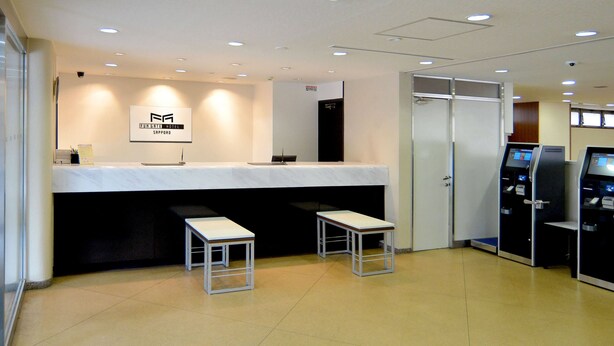 A hotel reception area with a marble counter, two small tables, a glass door, and a digital kiosk. - FUN GATE HOTEL SAPPORO (Sapporo)