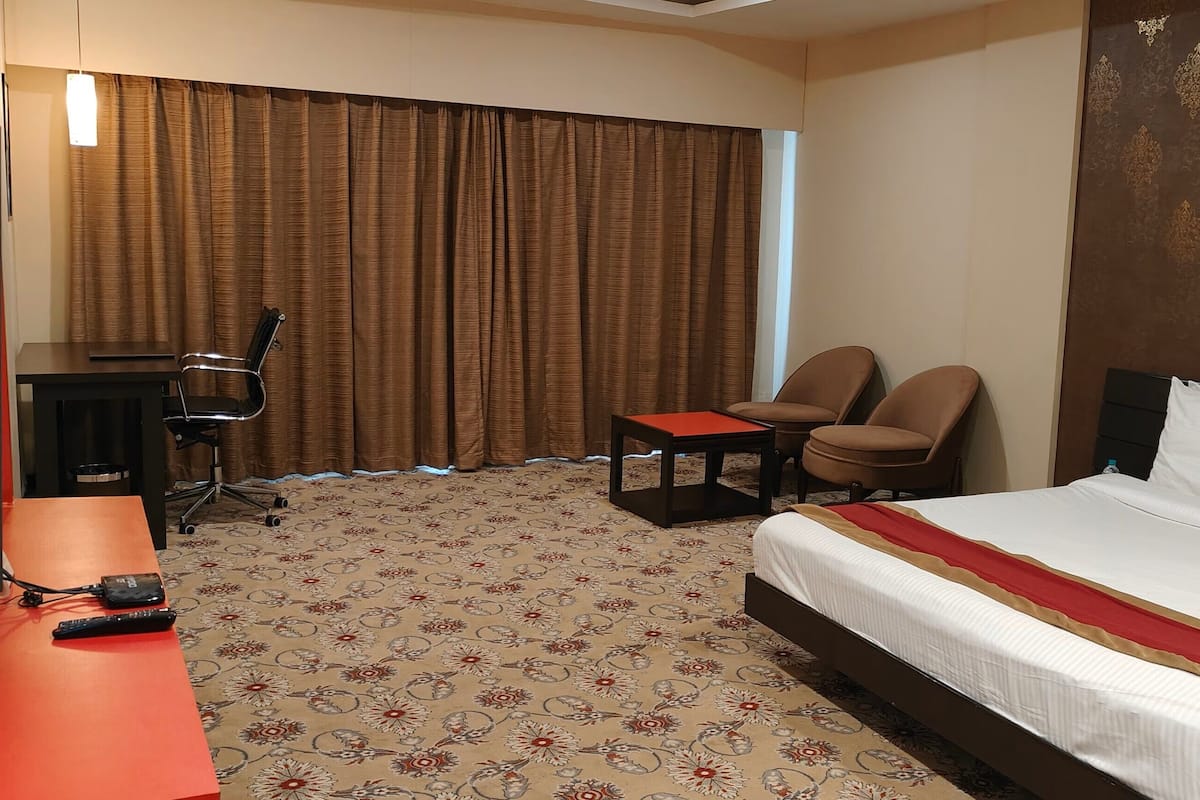 Ein Hotelzimmer mit einem Bett, zwei Sesseln, einem Schreibtisch, einem Fernseher und einem Vorhang.