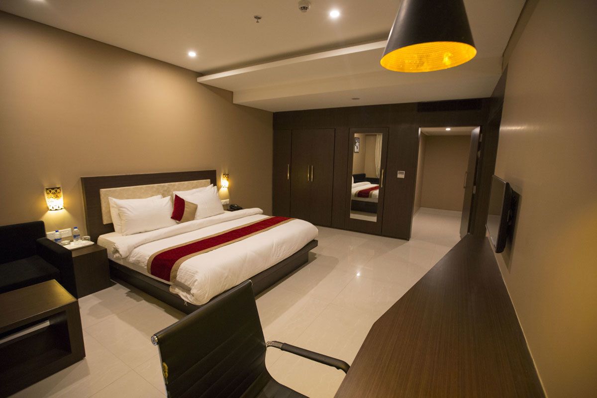 A modern hotel room with a large bed, bedside tables, a desk, and a wardrobe.