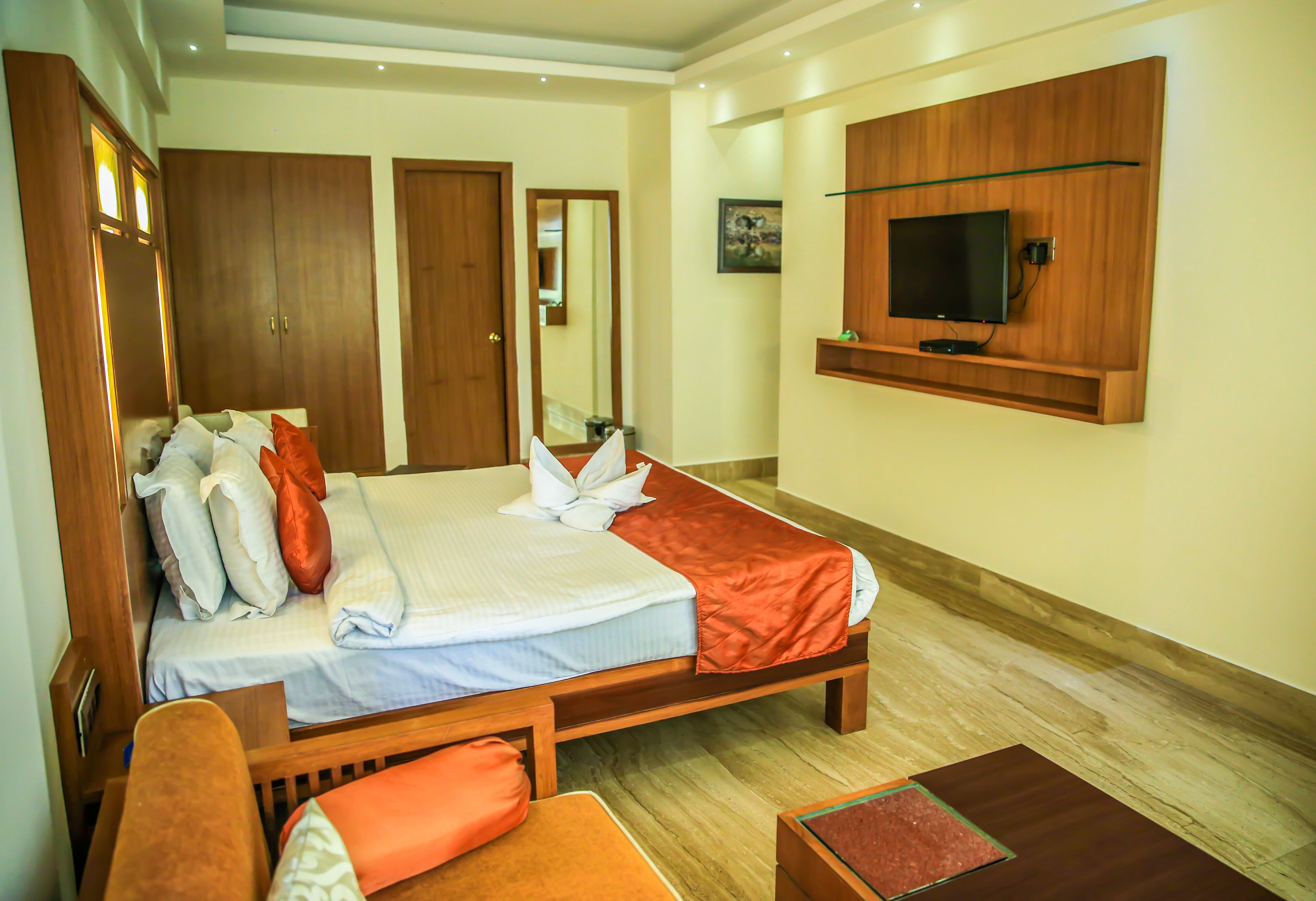 A hotel room with a large bed, wooden wardrobe, a television mounted on the wall, and a small seating area.