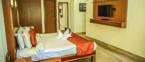 A hotel room with a large bed, wooden wardrobe, a television mounted on the wall, and a small seating area.