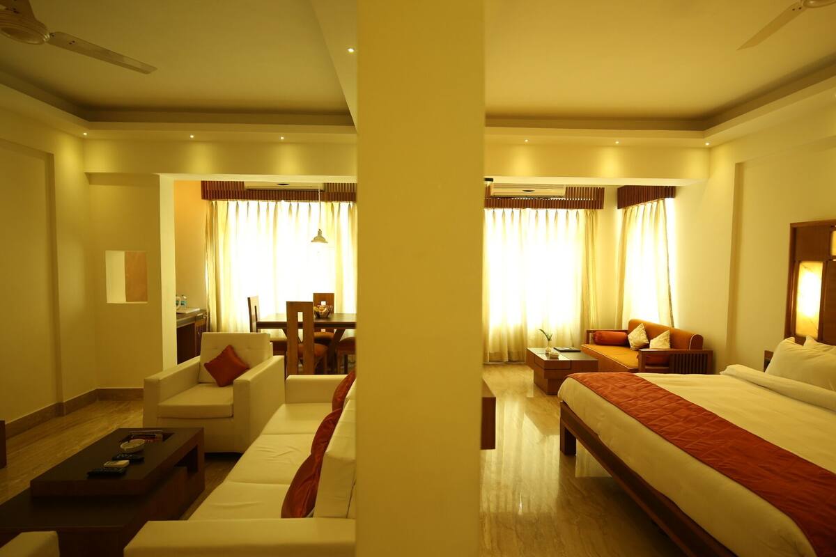 Habitación de hotel con cama, sofá, una mesita de centro y un comedor con mesa y sillas.