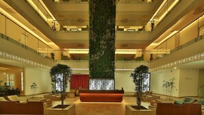 A spacious lobby with a central reception desk, multiple seating areas, and a large vertical garden.