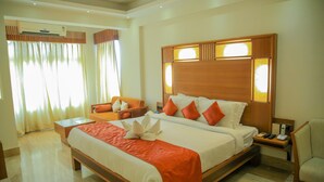 A spacious hotel room with a large bed, a bedside table, a chair, and a desk with a chair.
