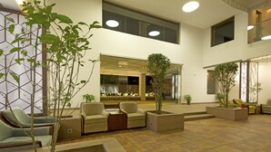 A spacious indoor area with multiple seating arrangements, including sofas and chairs, and several potted plants.