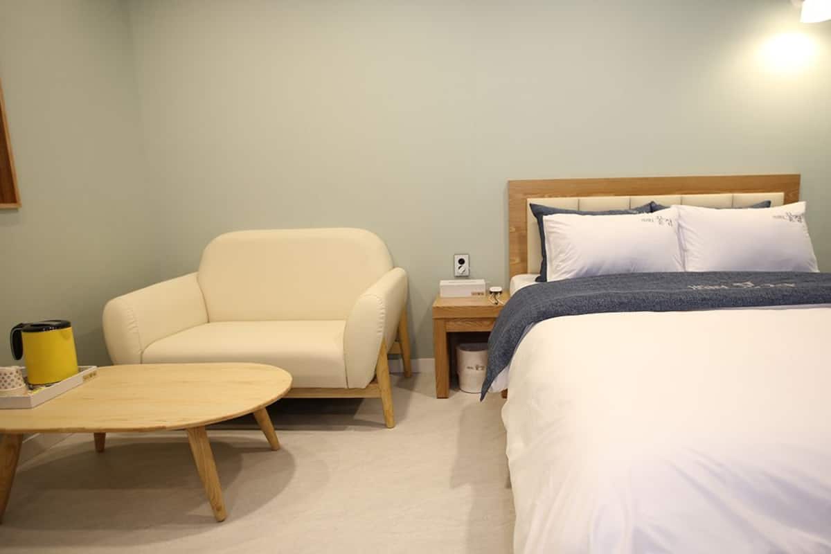 A hotel room with a bed, a chair, a bedside table, and a lamp.