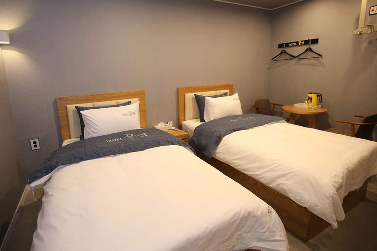 A hotel room with two single beds, a small table with a chair, and a wall-mounted coat rack.