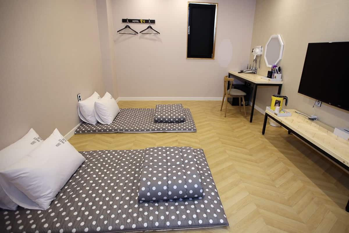 A room with two beds, a desk, a chair, a TV, and a mirror.