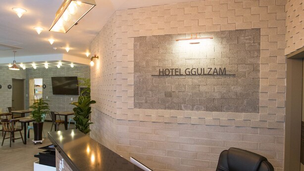 A hotel reception area with a modern design, featuring a reception desk, seating area, and a wall-mounted sign that reads "HOTEL GGULZAM". - Hotel Ggulzam (Yeosu)