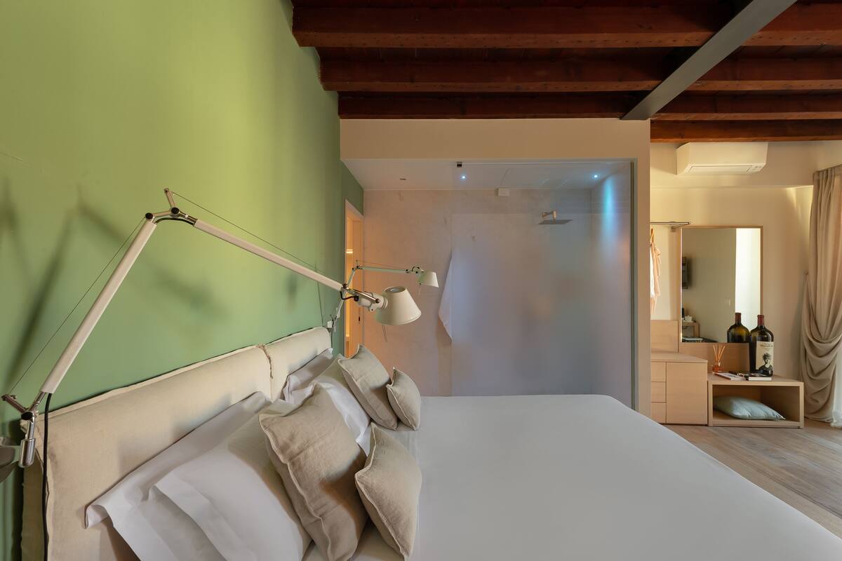 A bedroom with a bed, pillows, a bedside lamp, a mirror, and a wooden ceiling.