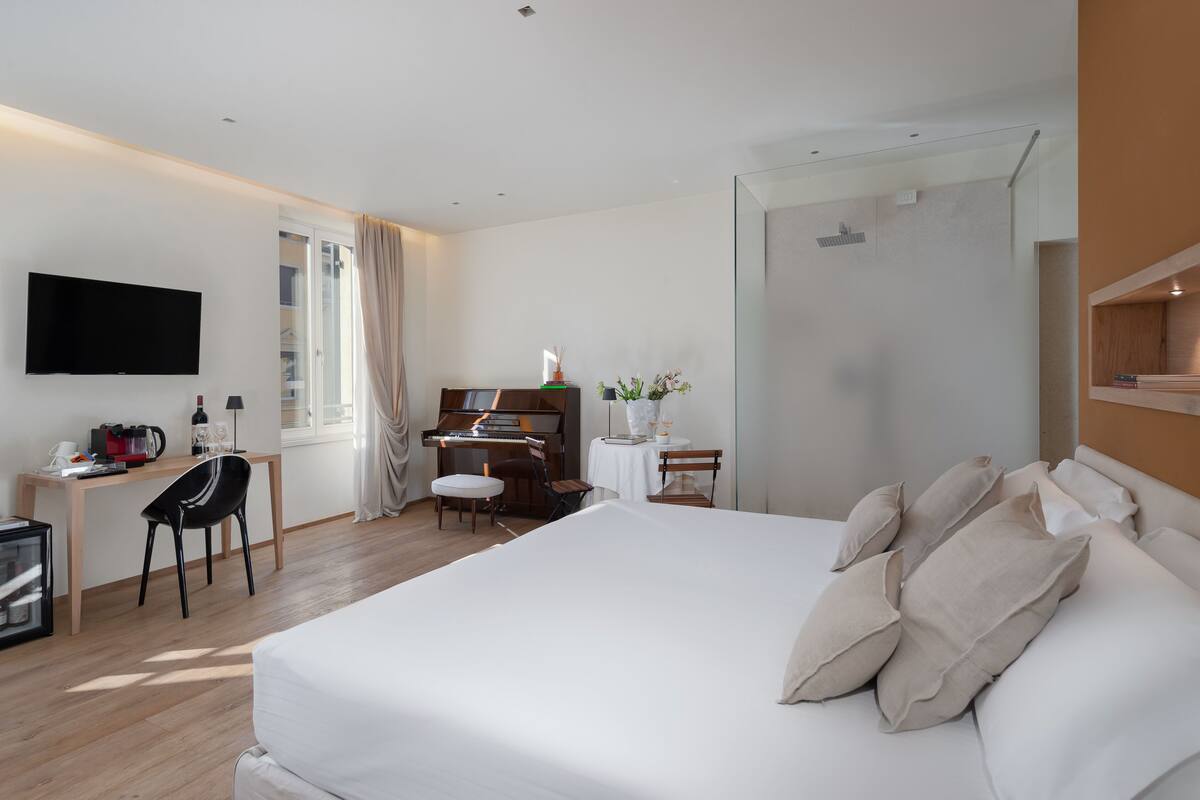 A hotel room with a bed, a desk with a computer, a television, and a piano.
