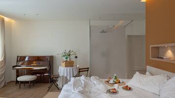 A hotel room with a piano, a bed with white linens, a breakfast tray, and a small table with a vase of flowers.