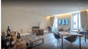 A modern living room with a sofa, coffee table, and a dining area with a table and chairs. There are wine bottles and glasses on the coffee table. - Massimago Wine Suites (Verona)