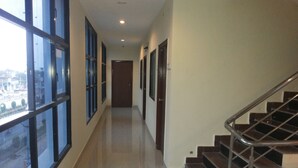 A corridor with a staircase on the right, large windows on the left, and a door at the end. - Hotel Neem Tree (Hyderabad)