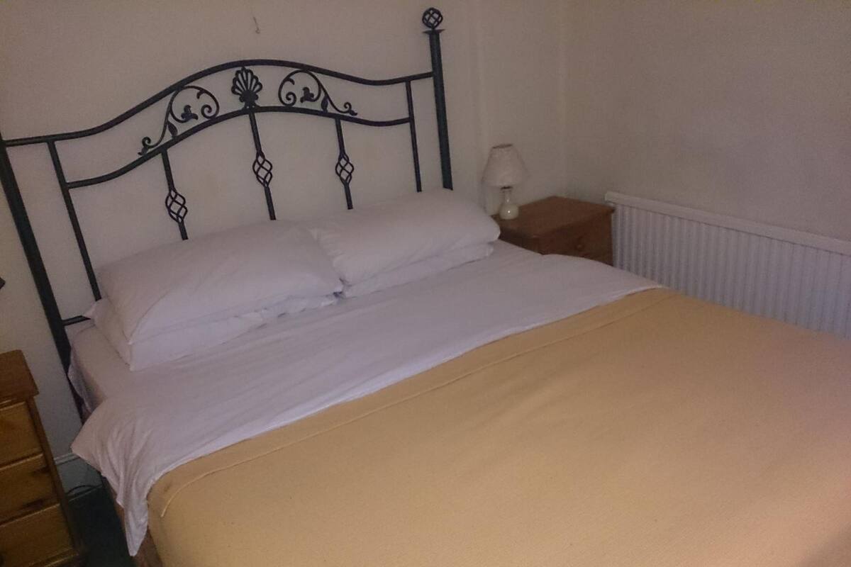 A single bed with a metal headboard, a bedside table with a lamp, and a radiator on the wall.